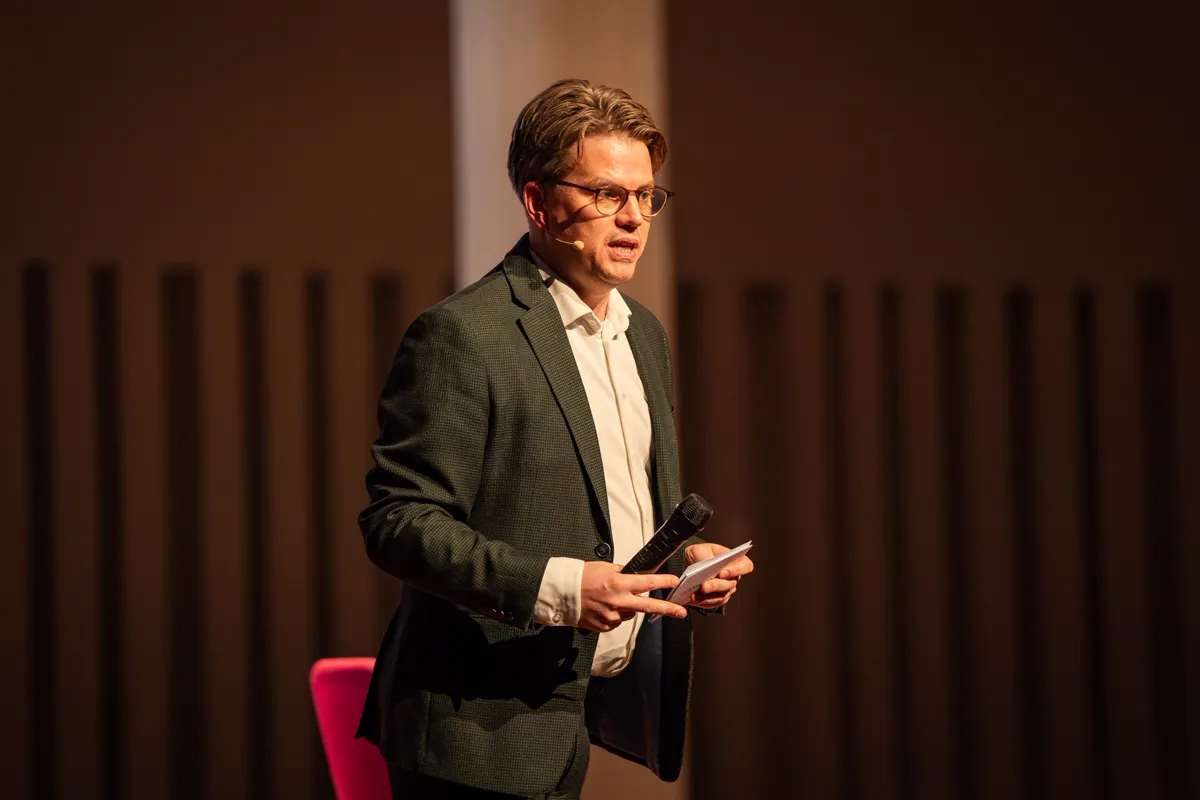 Jerre Maas met headset als dagvoorzitter op het podium van The Road
